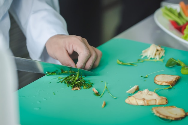 Disparo de cerca de un chef cortando verduras en alimentos va a cocinar en la cocina para servir comida a los clientes en el restaurante del hotel