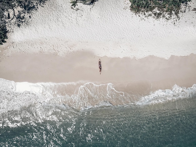 Disparo de drones de una mujer hermosa joven tumbada en la playa de arena blanca junto al agua clara; antecedentes. concepto de ocio.