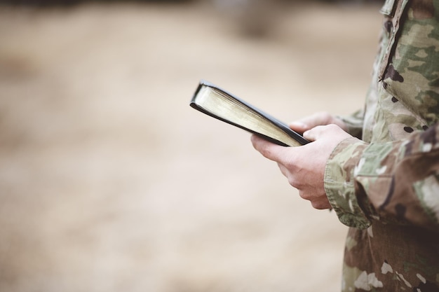 Disparo de enfoque superficial de un joven soldado sosteniendo una Biblia en un campo
