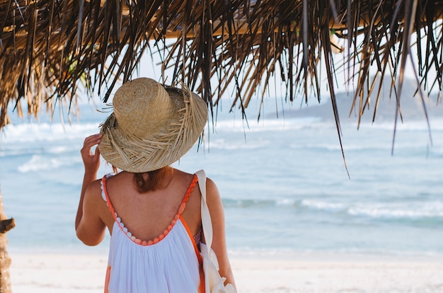 Foto disparo de enfoque superficial de una mujer con un vestido de verano mientras está de pie bajo un refugio en la playa