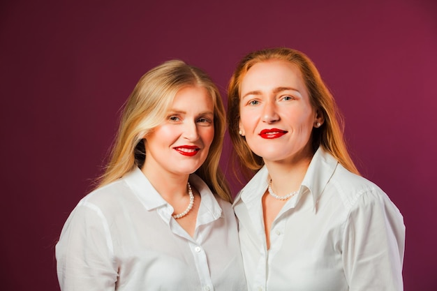 Disparo de estudio de dos hermosas hermanas rubia y pelirroja posando en camisas blancas Dos mujeres jóvenes con belleza natural sobre fondo púrpura