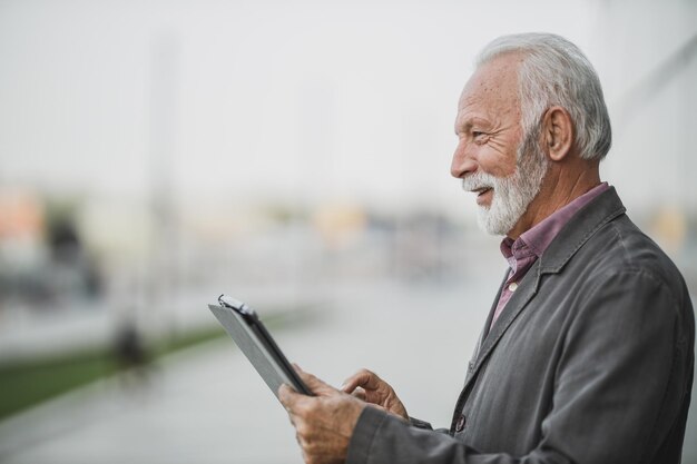 Disparo de un exitoso hombre de negocios senior usando tableta digital en la calle de la ciudad.