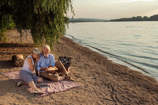 Disparo de una feliz pareja de ancianos haciendo un picnic en la orilla del río