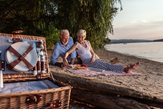 Disparo de una feliz pareja de ancianos haciendo un picnic en la orilla del río