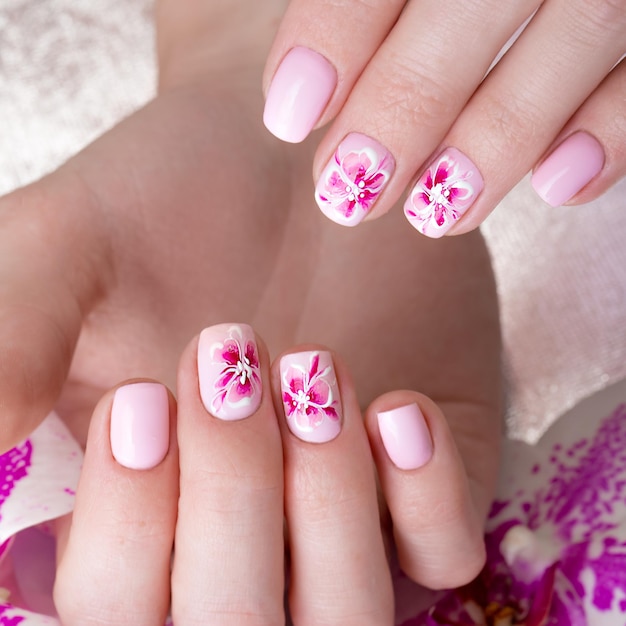 Disparo hermosa manicura con flores en los dedos femeninos Diseño de uñas Foto de primer plano tomada en el estudio sobre un fondo blanco