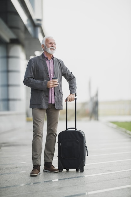 Disparo de un hombre de negocios senior caminando con su equipaje fuera del aeropuerto.