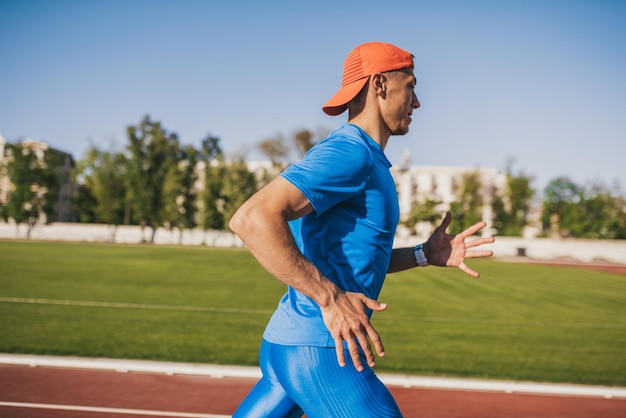 Disparo horizontal determinado atlético masculino caucásico joven corriendo solo a lo largo de una pista de carreras en el estadio mientras entrenaba en un día soleado Estilo de vida deportivo y concepto de personas