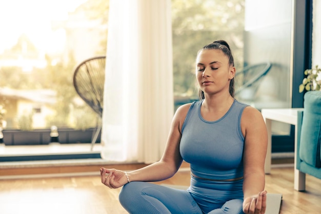 Disparo de una joven mujer linda meditando en la posición de loto en casa.