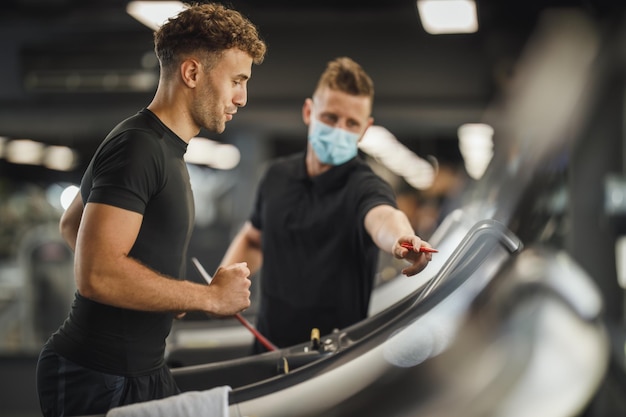 Disparo de un joven musculoso trotando en la cinta de correr en el gimnasio. Él está trabajando con un entrenador personal.