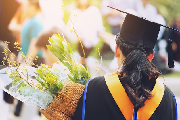 Disparo lado trasero joven estudiante en mano sosteniendo un ramo de flores durante la graduación en la universidad.