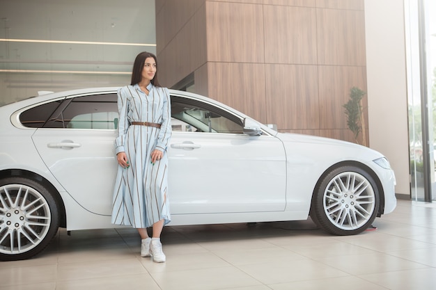 Disparo de longitud completa de una mujer elegante posando con su nuevo automóvil en el concesionario de automóviles, espacio de copia