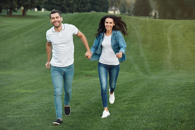 Disparo de longitud completa de pareja feliz corriendo sobre la hierba verde en el parque