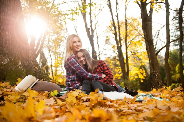 Disparo de una madre abrazando a su hija sentada en el bosque de otoño