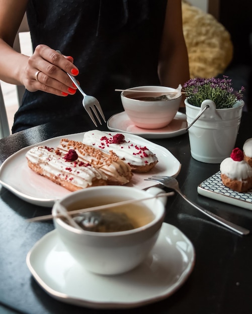 Disparo de mujeres tratando de comer eclairs de postre francés tradicional y beber té caliente en un café o restaurante