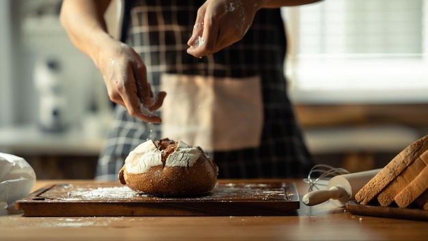 Disparo de panadero masculino rociando harina sobre masa fresca preparando pan en una cocina brillante