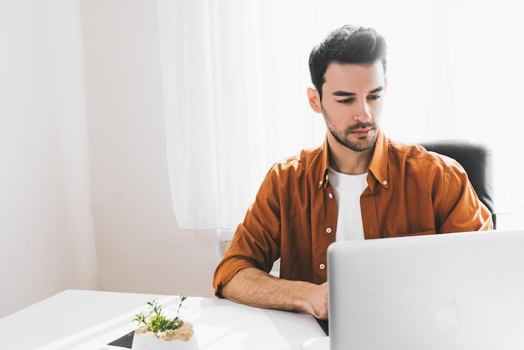 Foto disparo sincero de un joven gerente caucásico serio sentado en casa con una computadora portátil genérica escribiendo tratando de concentrarse en el trabajo que parece exhausto en el escritorio concepto de tecnología moderna de negocios de personas