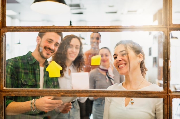 Disparo a través de la ventana del trabajo en equipo multirracial con feliz mirando pegatinas de post discutiendo