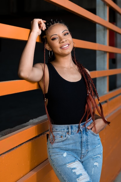 Foto disparo vertical de una alegre dama afroamericana con muertos apoyado en una construcción naranja