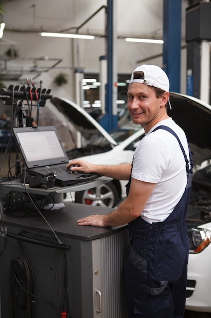 Disparo vertical de un alegre mecánico de automóviles con computadora en el garaje, reparación de automóviles