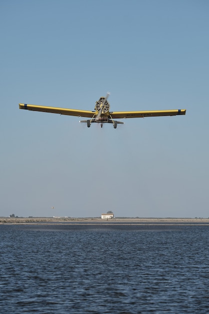 Disparo vertical de un avión monomotor vintage con una hélice volando sobre un paisaje agrícola