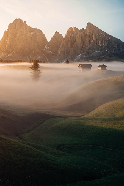 Disparo vertical de casas rurales y montañas rocosas durante un amanecer brumoso en Seiser Alm Tirol del Sur