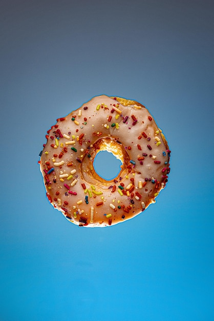 Disparo vertical de un donut con glaseado blanco y chispas de arco iris sobre un fondo azul