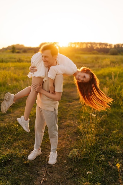 Disparo vertical de feliz joven pareja casada enamorada jugando disfrutando en el campo verde durante la puesta de sol dorada en la noche de verano