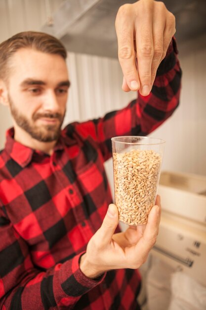 Foto disparo vertical de un guapo cervecero barbudo examinando semillas de cebada, trabajando en su fábrica de cerveza