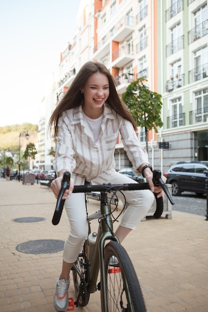 Disparo vertical de una hermosa mujer feliz riendo con entusiasmo, montando bicicleta en las calles de la ciudad
