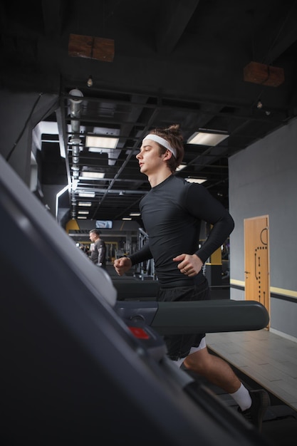 Foto disparo vertical de un hombre atlético guapo corriendo en la cinta de correr en el gimnasio