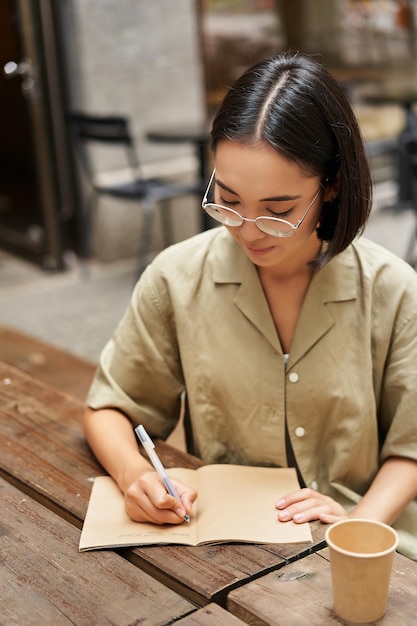 Foto disparo vertical de una joven asiática haciendo la tarea haciendo notas escribiendo algo sentado en un