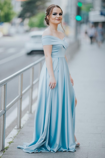 Disparo vertical de una joven caucásica vestida con un hermoso vestido de noche azul celeste hasta el suelo