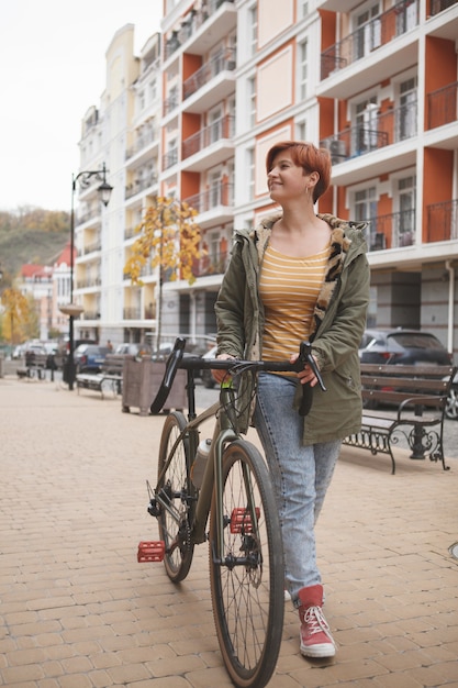 Disparo vertical de longitud completa de una mujer joven caminando por las calles de la ciudad con su bicicleta