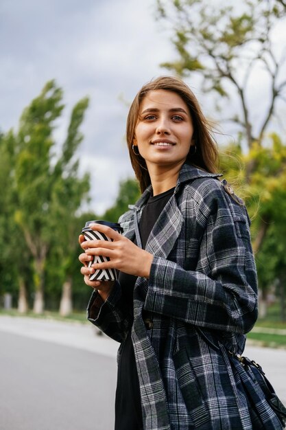 Disparo vertical de una mujer caminando sonriente mientras sostiene una taza de café de papel