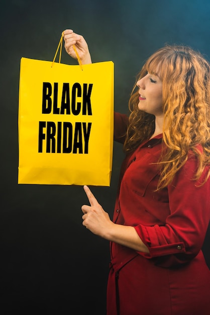 Foto disparo vertical de una mujer caucásica que muestra una bolsa de compras sobre un fondo negro viernes negro