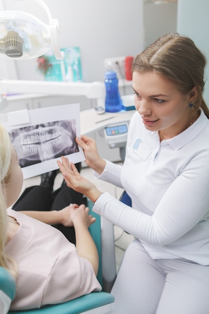 Disparo vertical de una mujer dentista que muestra la radiografía de la mandíbula a su paciente