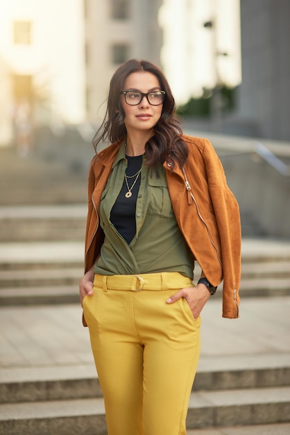 Disparo vertical de una mujer de negocios de moda confiada con anteojos mirando a un lado mientras