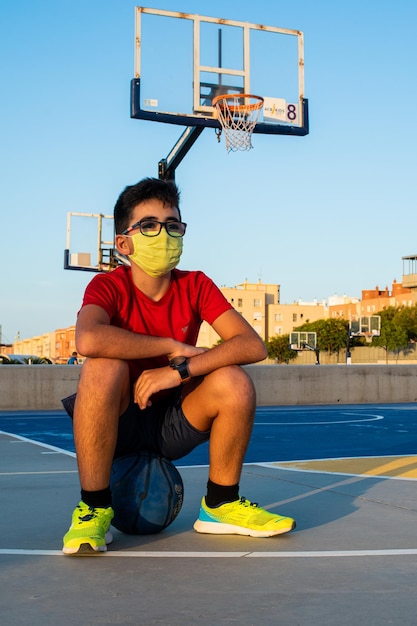 Disparo vertical de un niño sentado en una pelota con una máscara sanitaria: concepto de la nueva normalidad