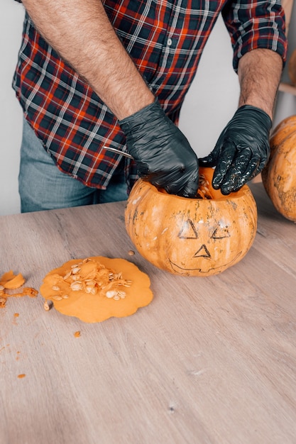 Foto un disparo vertical de una persona con guantes y tallando una calabaza para halloween