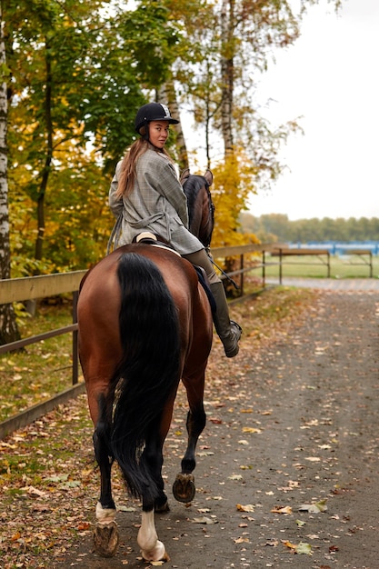 Disparo de vista trasera Retrato de una mujer joven y bonita con un día de otoño de equitación marrón
