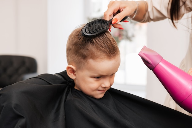 Disparos en un salón de belleza. El peluquero hace el peinado del niño con un secador de pelo y un peine.