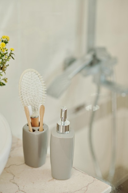 Dispensador de sabonete líquido e copo com escovas de dentes ao lado da pia no banheiro