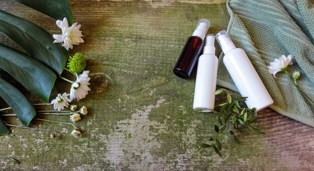 Foto dispensador de spray cosmético y flores sobre un fondo de madera