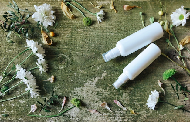 Foto dispensador de spray cosmético y flores sobre un fondo de madera