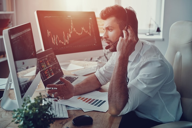 Disponible todo el día. Joven empresario en auriculares hablando con el cliente mientras está sentado en la oficina