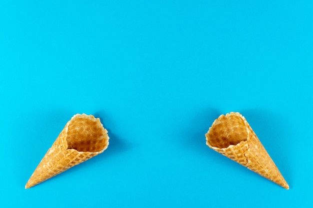 Disposição criativa do verão feita de cones de gelado, cones do waffle na luz brilhante - fundo azul.