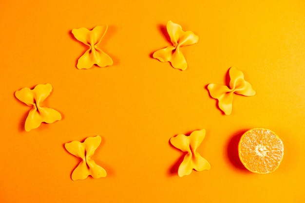 Disposición creativa de verano hecha de clementinas y papillon de sémola de pasta coloreada sobre fondo naranja