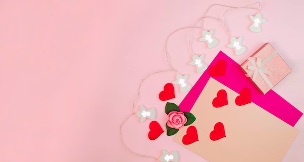 Disposición festiva. Una postal para San Valentín, Cumpleaños, Día de la Mujer o Día de la Madre. Corazones de papel rojo, una caja de regalo sobre un fondo rosa pastel. Diseño plano, vista superior, lugar para copiar.