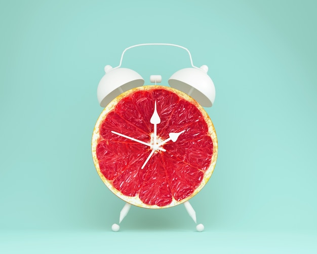 Disposición de idea creativa fresca pomelo rebanada despertador sobre fondo azul. fruta mínima