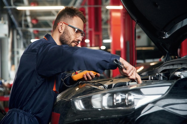 Dispositivo eléctrico profesional en manos El reparador de automóviles está en el garaje con el automóvil